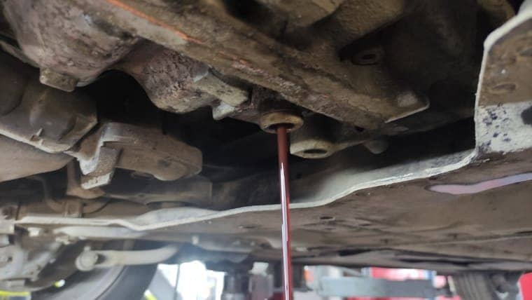 Запускаем двигатель автомобиля, переключаем передачи, задерживаясь на каждой на 2–3 секунды и откручиваем уровневую заглушку. Масло должно вытекать до отдельных капель.