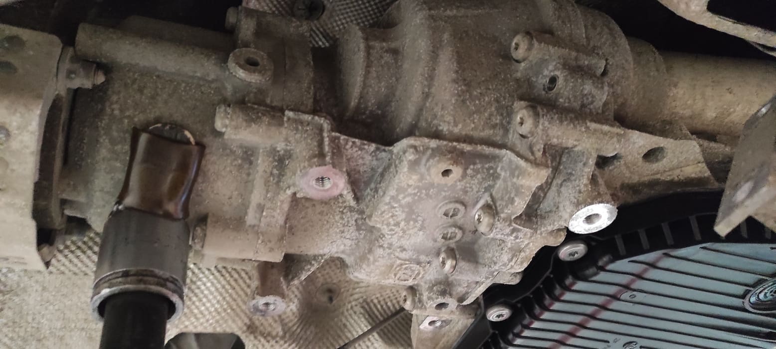 Дифференциал Torsen находится позади АКПП. Для замены старого масла из дифференциала Torsen необходимо открутить сливную и заливную пробки. На фото отчетливо видна заливная пробка. Чуть выше и правее опорной стойки (направление на 13 часов). Сливное отверстие хорошо видно на следующем фото.